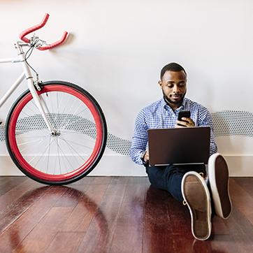 一个人拿着电话和电脑坐在自行车旁边